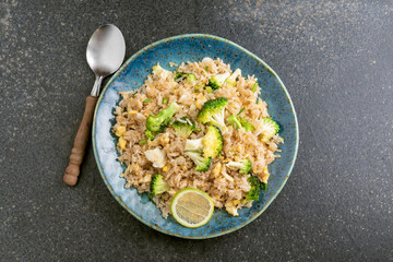 Vegetarian healthy food fried rice with broccoli egg in plate on black stone background.