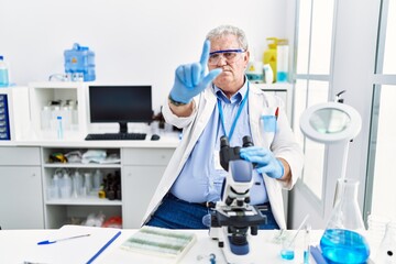 Senior caucasian man working at scientist laboratory pointing with finger up and angry expression, showing no gesture
