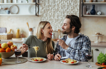 Smiling caucasian young male with stubble feeds blonde woman, couple have fun together in light...