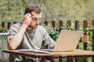Attractive adult man in eyeglasses looking at laptop display while sitting outdoors.