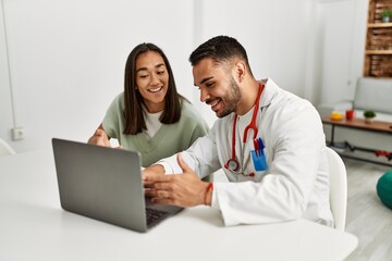 Doctor explain treatment to latin woman using laptop at clinic.