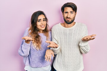 Young hispanic couple wearing casual clothes clueless and confused with open arms, no idea concept.