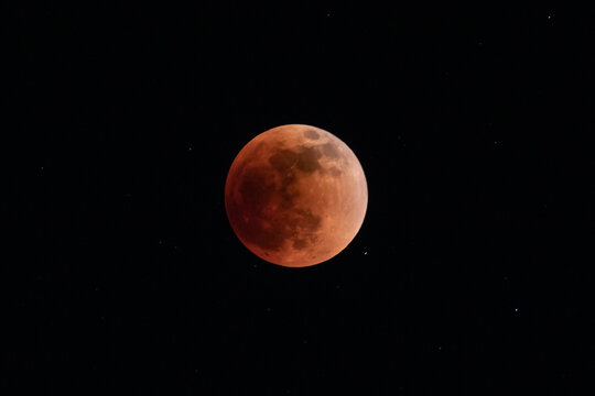 Full moon (blood moon) at the height of a lunar eclipse. Deep red color. Black sky and stars in background. 
