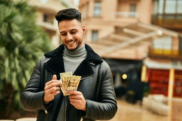 Young arab man smiling happy counting usa dollars at the city.