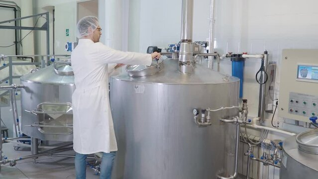 Worker is controlling the alcoholic drink brewing process at the plant. Worker is supervising the beer brewing process. Worker is looking inside of the mash tun during the beer brewing process.