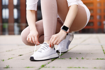 Close up woman beginner runner tie laces on sneakers, sitting on feet, on city street with building...