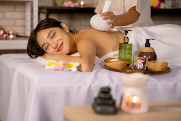 Obraz na płótnie Canvas Beautiful Asian woman lie on bed and close eyes with happiness during spa with herbal compress ball and foreground with several accessories of spa process.