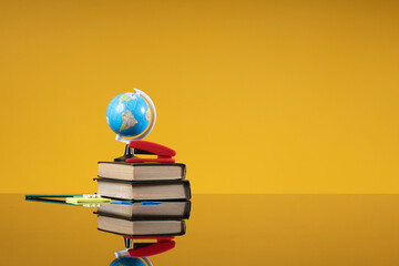 School accessories as a back to school concept. Globe and stapler on stack of old books and brush...