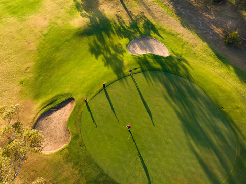 Drone shot of young male multiracial friends playing golf on grassy land at golf course at sunset