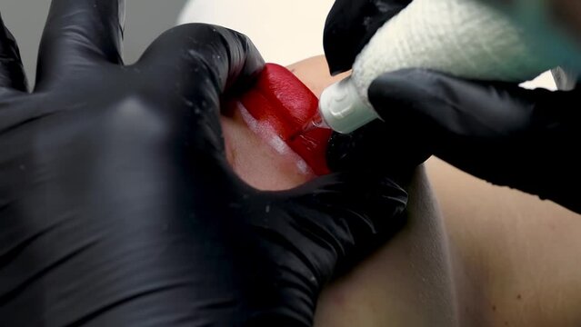 a close-up of the permanent lip makeup procedure of the master applies a tattoo on the red lips using a tattoo machine