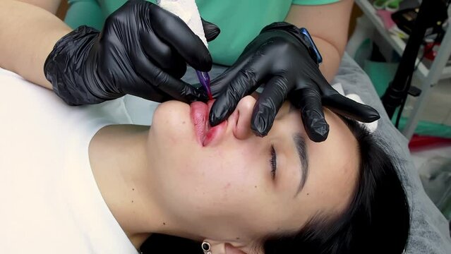 permanent lip makeup is performed by a master demonstrate it on a model of a brunette girl