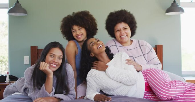 Portrait of happy diverse female friends lying on bed and smiling in bedroom