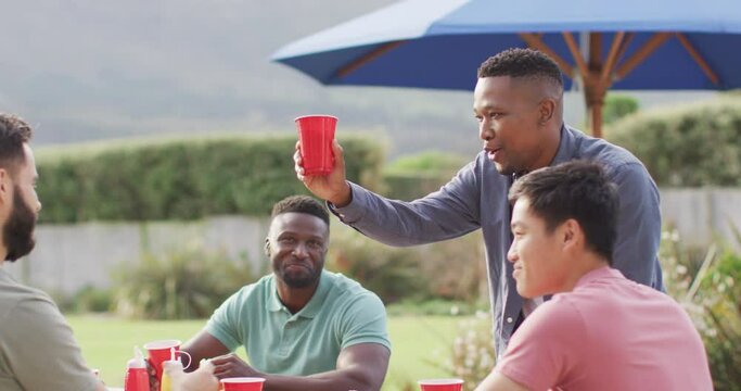 Happy diverse male friends talking and drinking beer in garden on sunny day