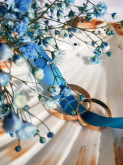 Two gold wedding rings intertwined with a turquoise ribbon lie on a beautiful shell. Gold rings in a shell on a white fabric background with turquoise gypsophila flowers. Close-up of gold wedding