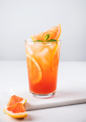 Fresh grapefruit juice with ice, mint and grapefruit slice in a glass on a white marble background with citrus  slices close up. Front view