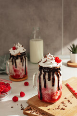 Two raspberry milkshakes with whipped cream and chocolate served in jars.