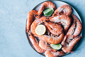 Ocean king prawns or jumbo shrimps with lemon slices in plate on grey background