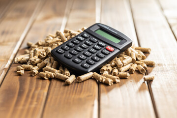 Wooden pellets and calculator, biofuel on wooden table. Ecologic fuel made from biomass. Renewable...