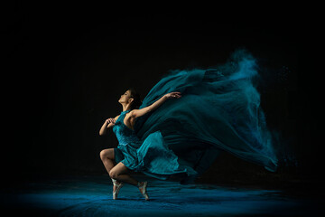 Emotional Southeast Asian ballet dancer in a green dress performing a move on a black background - obrazy, fototapety, plakaty
