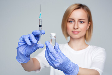 Blonde woman researcher holding liquid medicine drug and syringe in hands in blue gloves, disease...