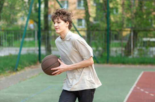 Cute young teenager in white t shirt with a ball plays basketball on court. Sports, hobby, active lifestyle for boys	