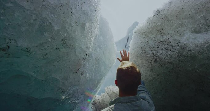 Man puts his hand on glacier and looks up at the Tustumena glacier in Kenai, Alaska