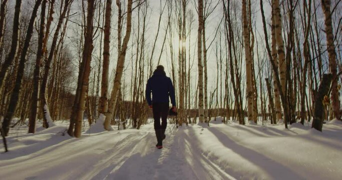 Man walks down snowy path inbetween trees in the Kenai National Wildlife Refuge, Alaska