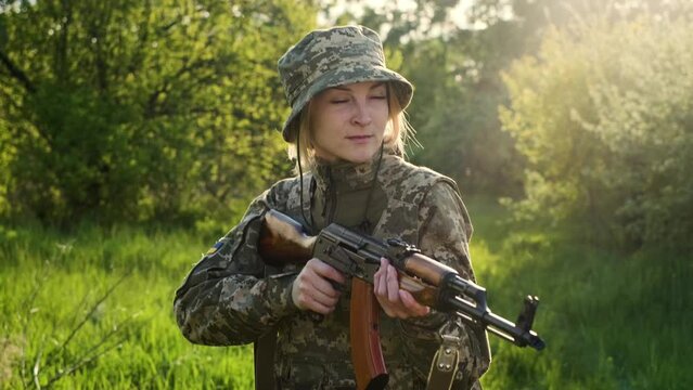 Young Ukrainian female soldier in camouflage uniform with an assault rifle in reconnaissance patrols a combat zone. Brave military patriot woman with a gun in the forest at sunset