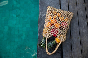 Mesh shopping bag with organic pineapple, orange, dragon, passion fruits on concrete background. Flat lay