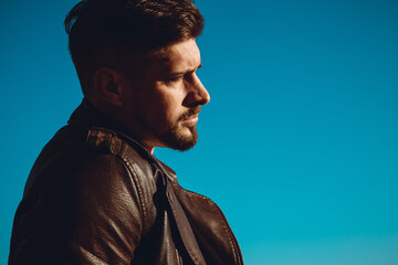 Portrait of handsome young man with stylish haircut and beard in a leather jacket posing on the rocks.