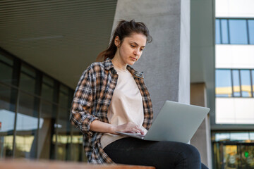 Front view. A girl in a shirt with a laptop on the street working. Remote work. c
Сonducting...