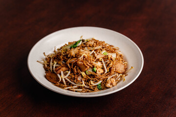 Closeup shot of a stir fried noodles  in a white plate on a wooden table