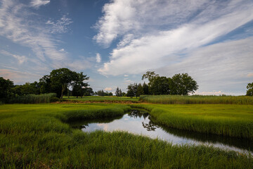 A Golf course in Rhode Island and a small Pond between green grass and a blue cloudy sky