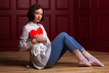 Short-haired woman sitting side to camera on floor holding heart shape on chest
