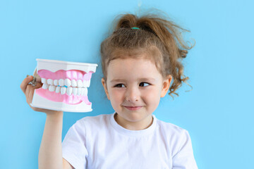Little cute funny girl holding tooth jaw. Kid training oral hygiene. Child learning brushing,...