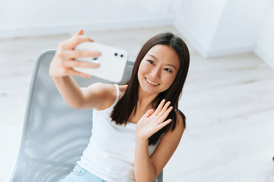 Enjoyed smiling tanned lovely young Asian woman waving hand greeting friend on live doing selfie video call at home. Distance communication Social media concept. Cool offer Banner Wide angle