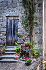 Fototapeta na wymiar Old black wooden door in a stone wall with steps and flower pots