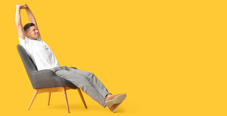 Young man relaxing in armchair against yellow background with space for text
