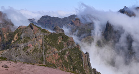 Panorama from Pico do Areeiro, a starting point of PR1 trail in Madeira Island. Hikers on trail to Pico Ruivo, the highest in Madeira. Fog ascending from a valley and remaining among mountain folds.