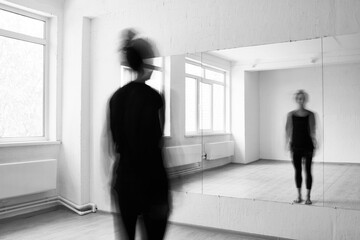 Black and white photo of woman standing in front of mirror in dancing studio, blurred motion