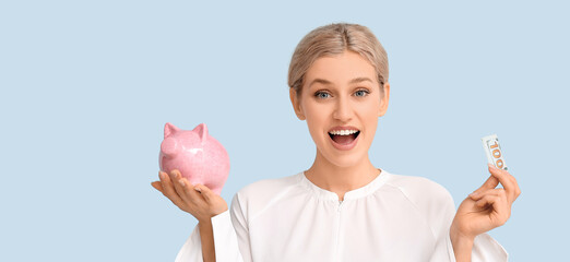 Happy young woman with piggy bank and money on light blue background