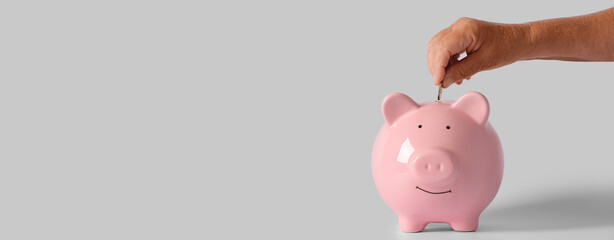 Hand of senior woman putting coin into piggy bank on light background with space for text - obrazy, fototapety, plakaty