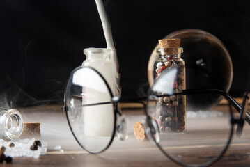 Small glasses with cork stopper with spices and empty, smoke, and more accessories, black background, selective focus.