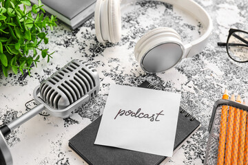 Microphone, headphones, notebook and sheet of paper with word PODCAST on grunge background, closeup