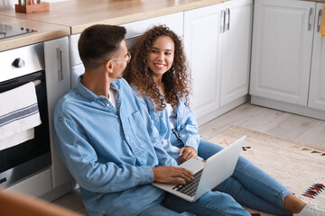 Young couple using laptop on floor in kitchen