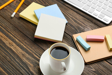 Obraz na płótnie Canvas Cup of coffee, blank sticky notes, notebook, keyboard and stationery supplies on wooden table, closeup