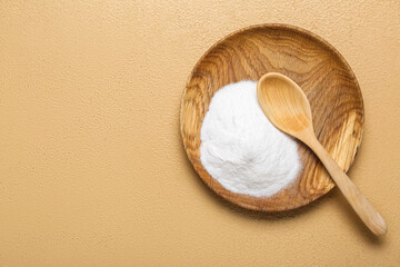Plate with baking soda and spoon on beige background