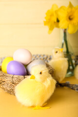 Cute chickens, nest with Easter eggs and flowers on table