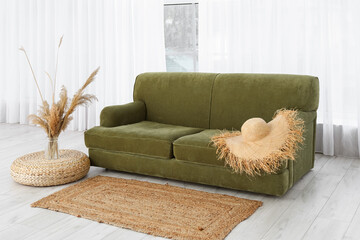 Comfortable sofa, wicker hat and vase with pampas grass near big window in living room