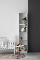 Interior of light nursery with baby crib, table and shelving unit